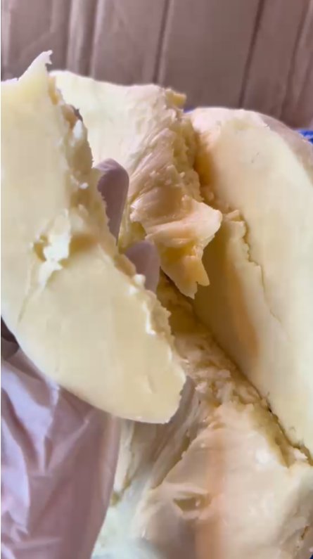 Morceau de beurre de karité brut, texture riche et granuleuse, couleur ivoire.